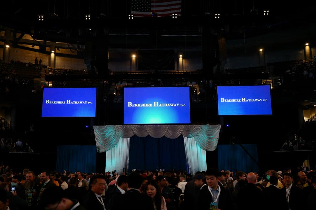 The arena floor at the Berkshire Hathaway annual shareholder meeting, three large screens reading 'Berkshire Hathaway Inc.' above a crowd